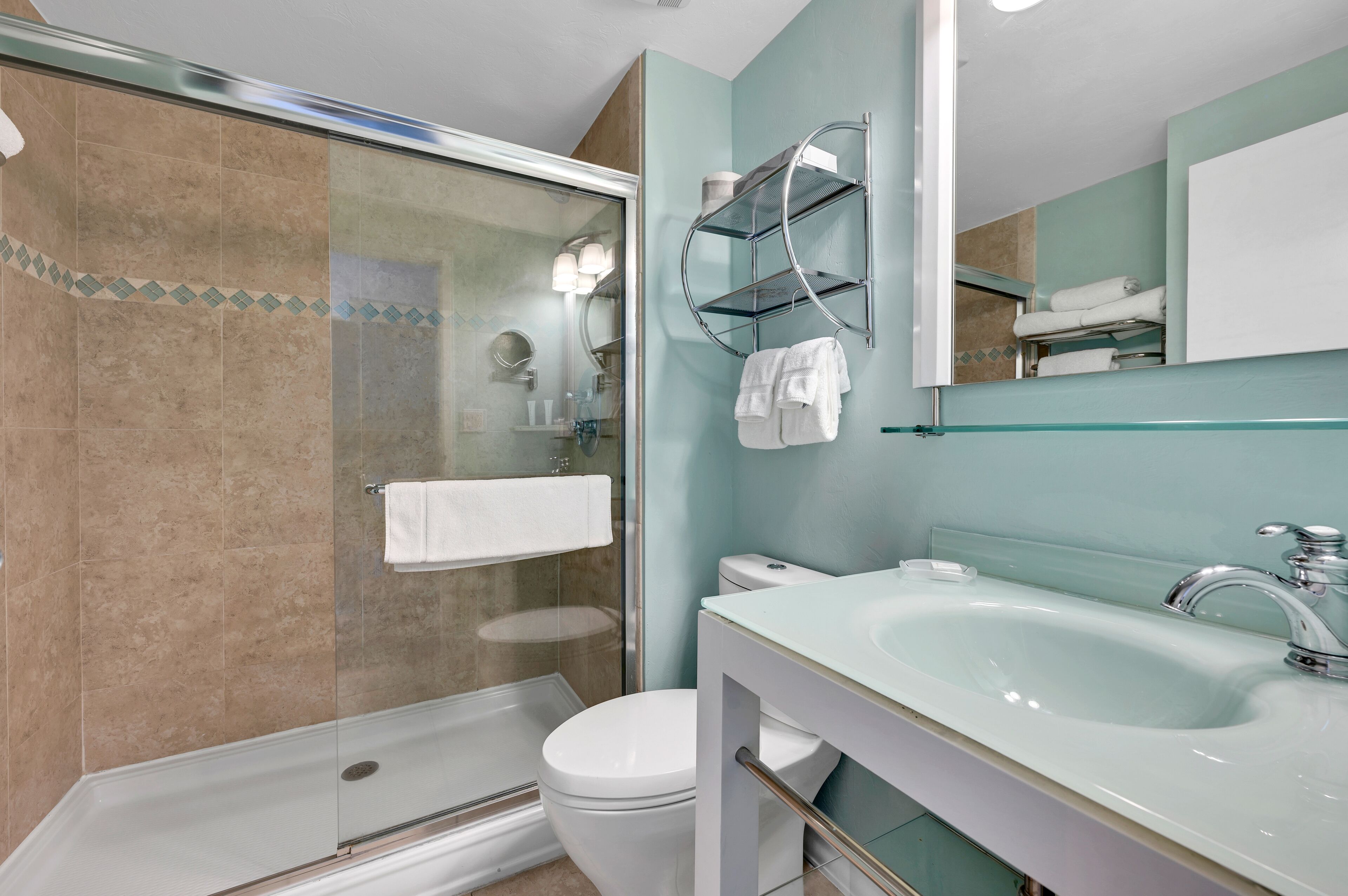 Ein modernes Badezimmer mit einer Duschkabine, einer weißen Toilette, einem Waschbecken mit Chromarmatur und einem Spiegel über dem Waschbecken.
