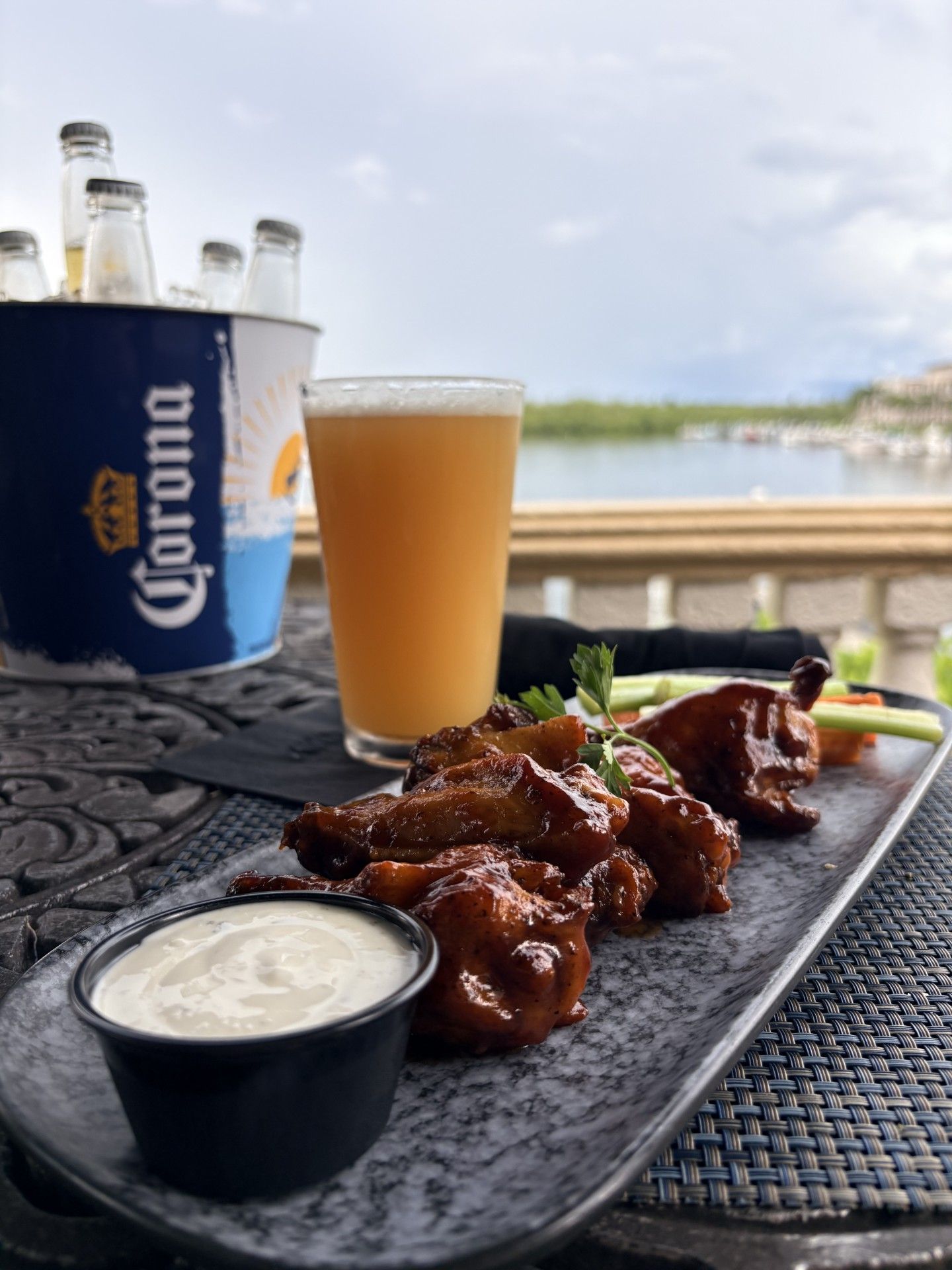 A meal with ribs, a glass of beer, and a Corona beer bottle on a table with a view of a body of water.
