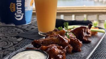 A meal with ribs, a glass of beer, and a Corona beer bottle on a table with a view of a body of water.