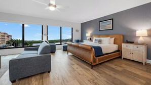 A modern bedroom with a large bed, a sofa, a nightstand, and a view of the city. - Bayfront Inn Fifth Avenue (Naples)