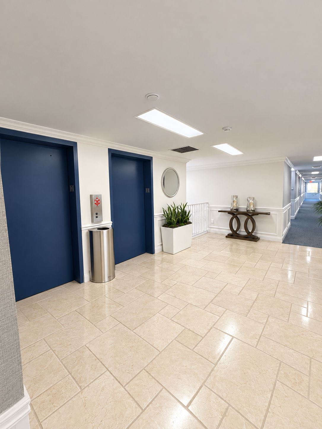 A hotel lobby with a reception desk, a trash can, a potted plant, and a wall-mounted mirror.