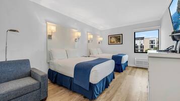 A hotel room with two beds, a sofa, a desk, and a large window with a view of buildings.