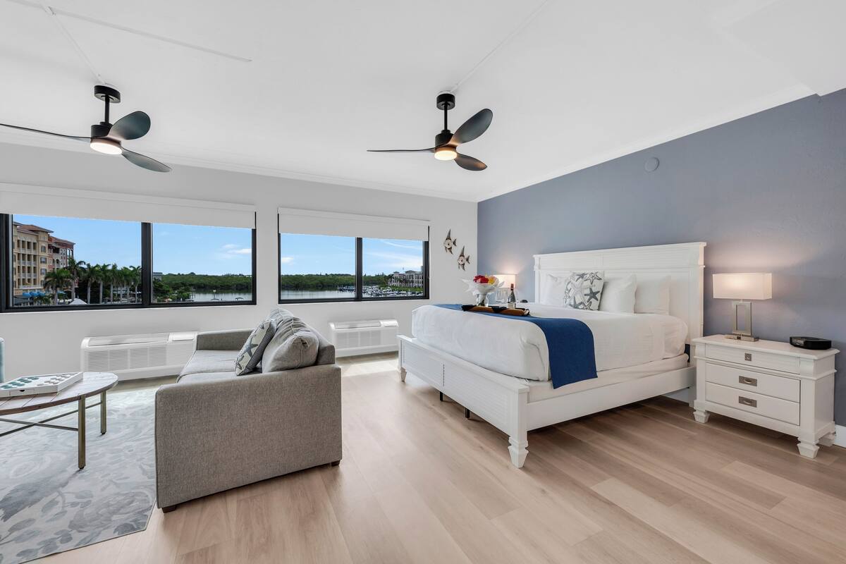 A modern bedroom with a large bed, a sofa, a coffee table, and two ceiling fans.