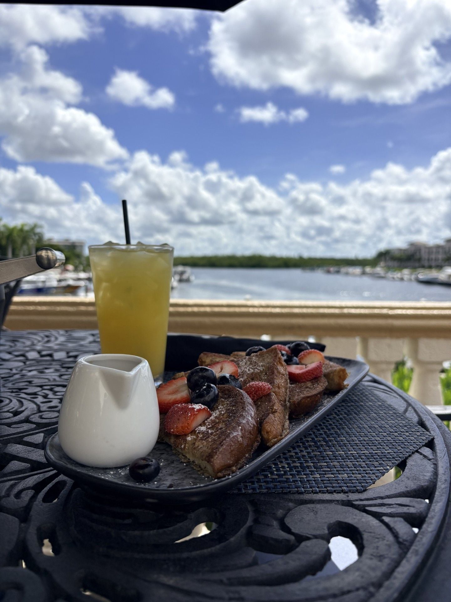 Un plato de waffles con fruta y una bebida sobre una mesa, con vista al agua y al cielo.