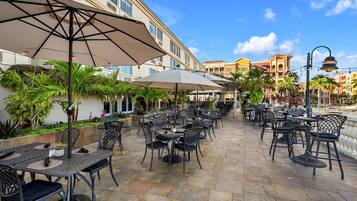Un patio al aire libre con varias mesas y sillas, sombrillas y vistas a un edificio con balcones.