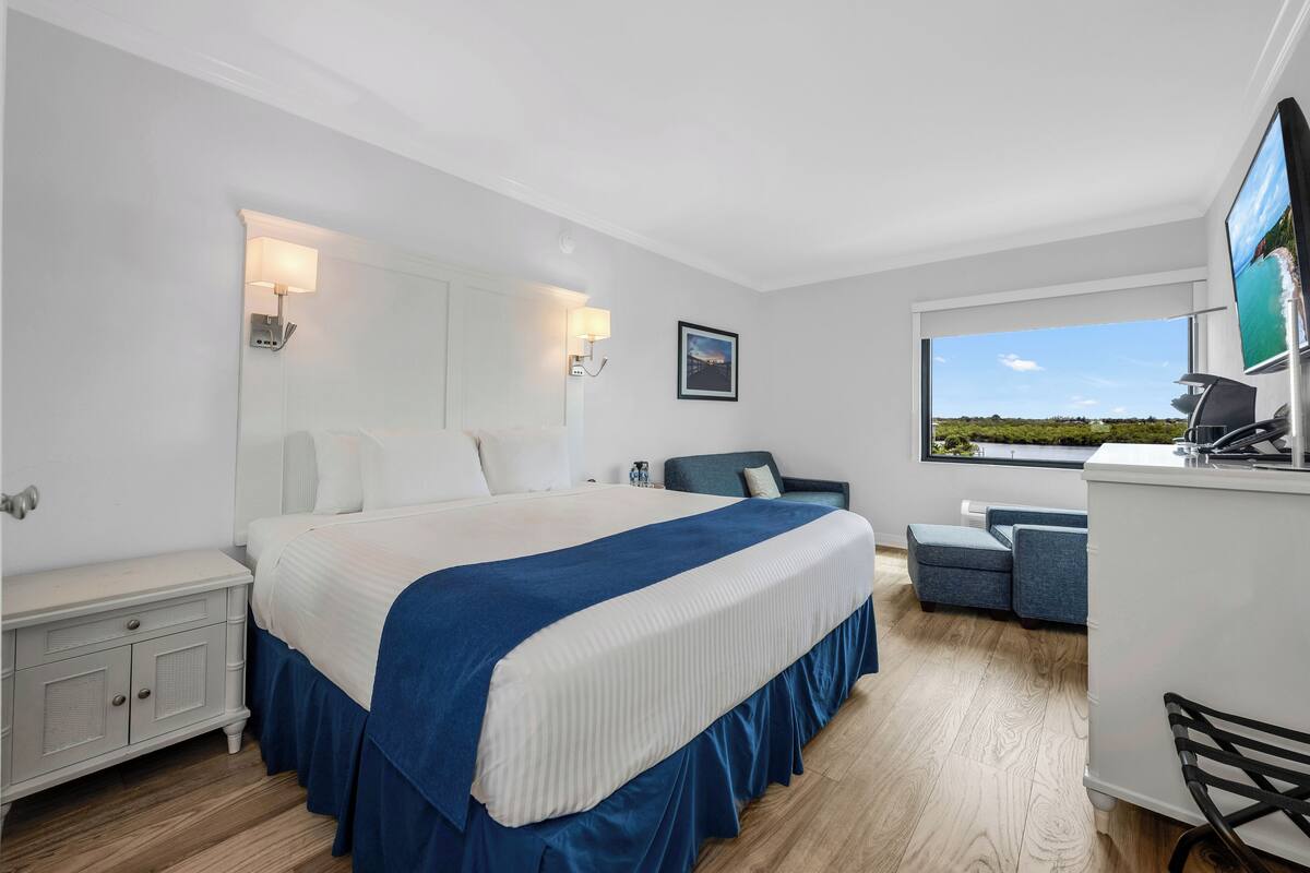 A modern hotel room with a large bed, a desk, and a view of the outdoors.