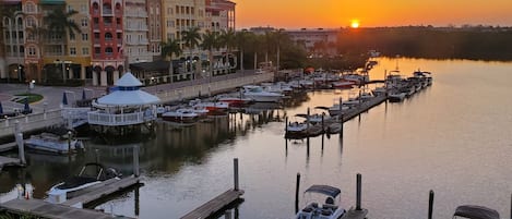 A marina with boats docked, a waterfront promenade with outdoor seating, and multi-story buildings in the background.