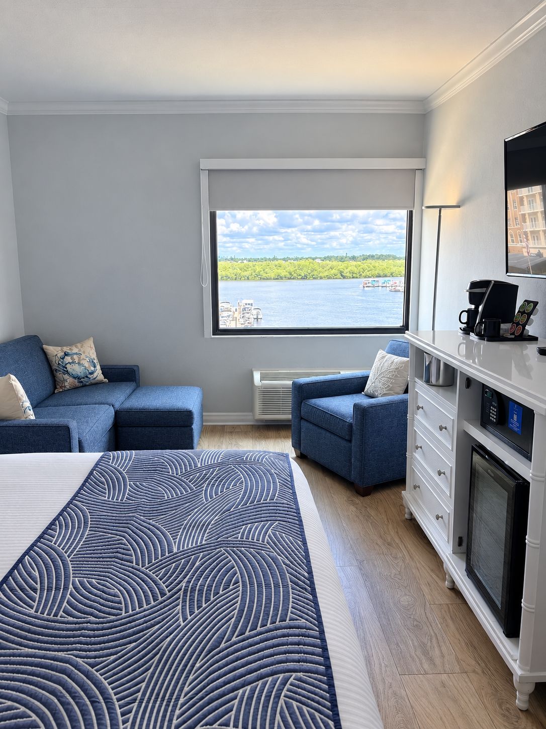 Een hotelkamer met een bed, twee slaapbanken, een koffiehoek en uitzicht op een waterpartij.