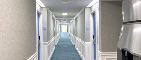 A hotel corridor with a blue carpet, white walls, and a stainless steel refrigerator.