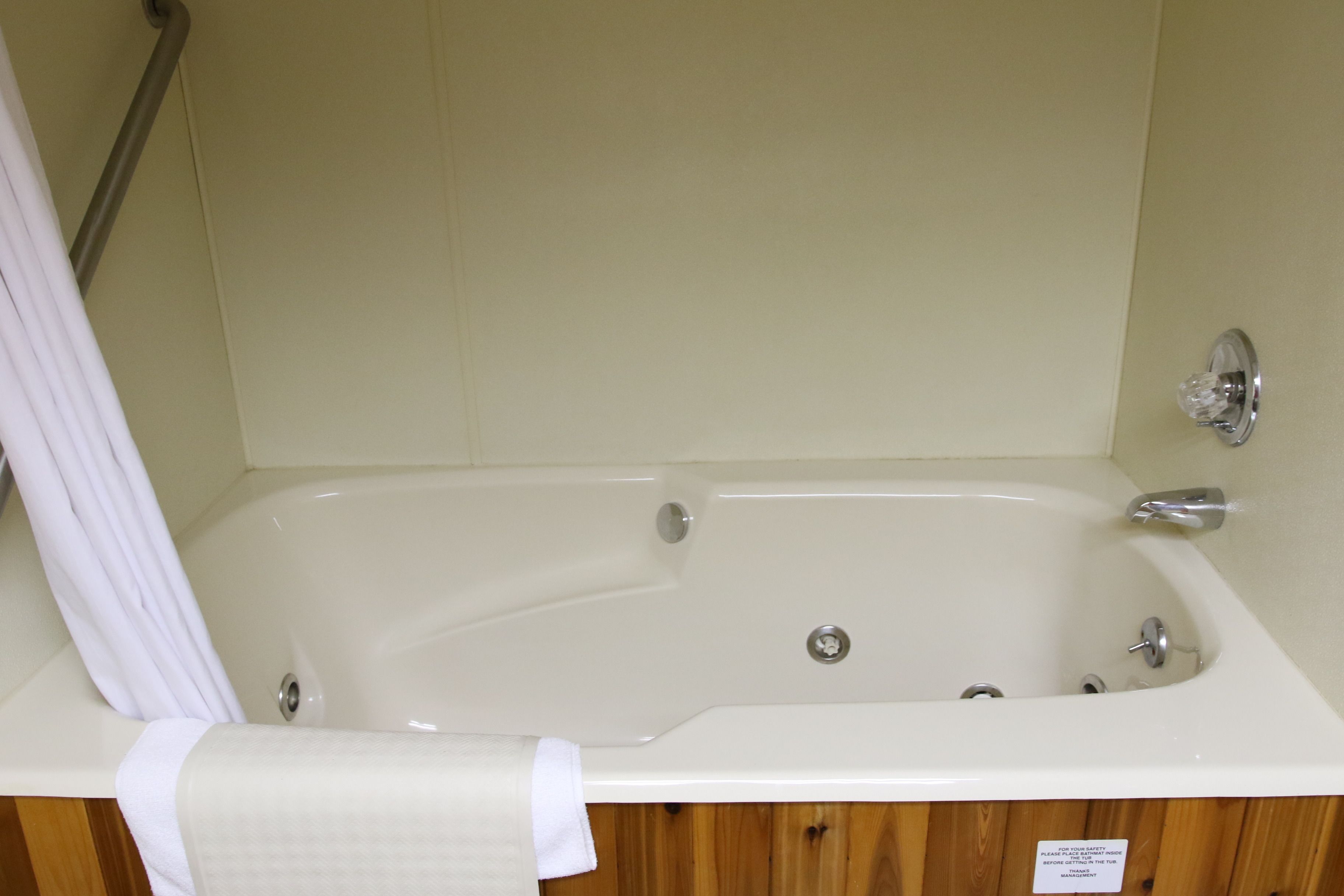 A white bathtub with a shower curtain, wooden paneling, and a sign indicating the room is for guests with disabilities.