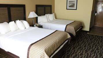Quarto de hotel com duas camas, uma mesa de cabeceira com abajur, um quadro na parede e um tapete estampado.