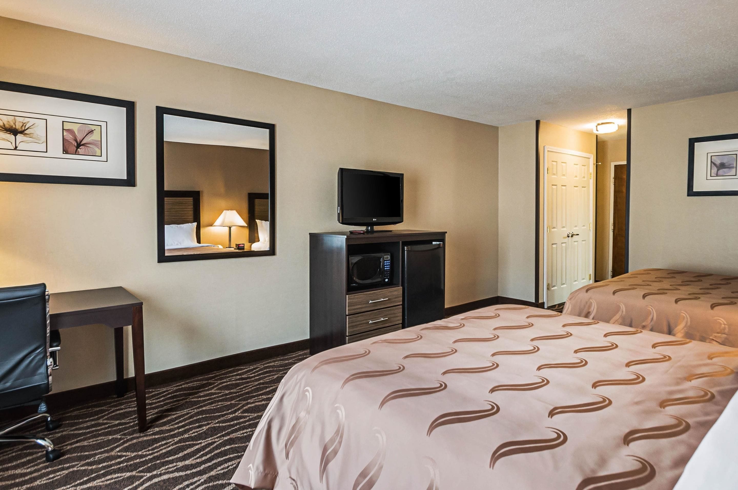 A hotel room with two beds, a desk, a television, a microwave, and a mirror.