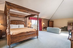 A four-poster bed with a wooden headboard, a sofa, a cabinet, and a window with curtains. - Quality Inn & Suites Frostburg - Cumberland (Frostburg)