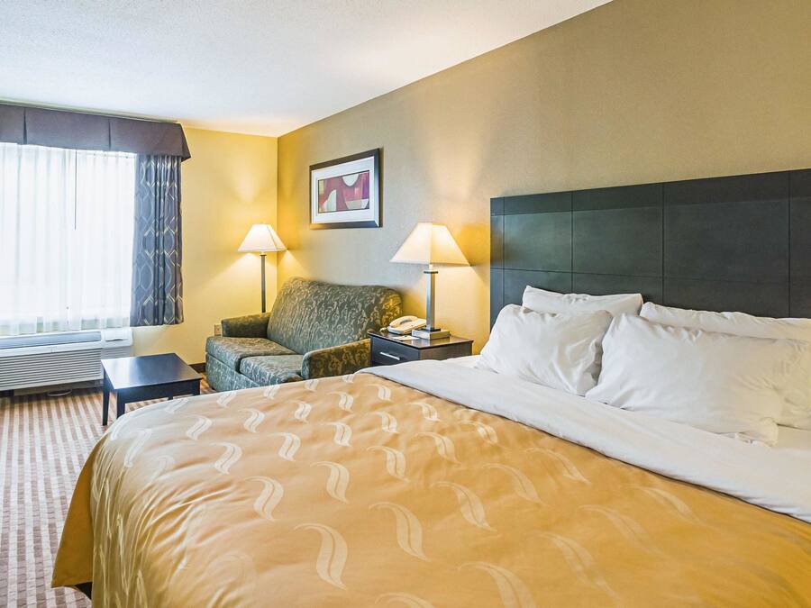 Camera d'albergo con un letto grande, due abat-jour, una sedia, una scrivania e una finestra con tende.