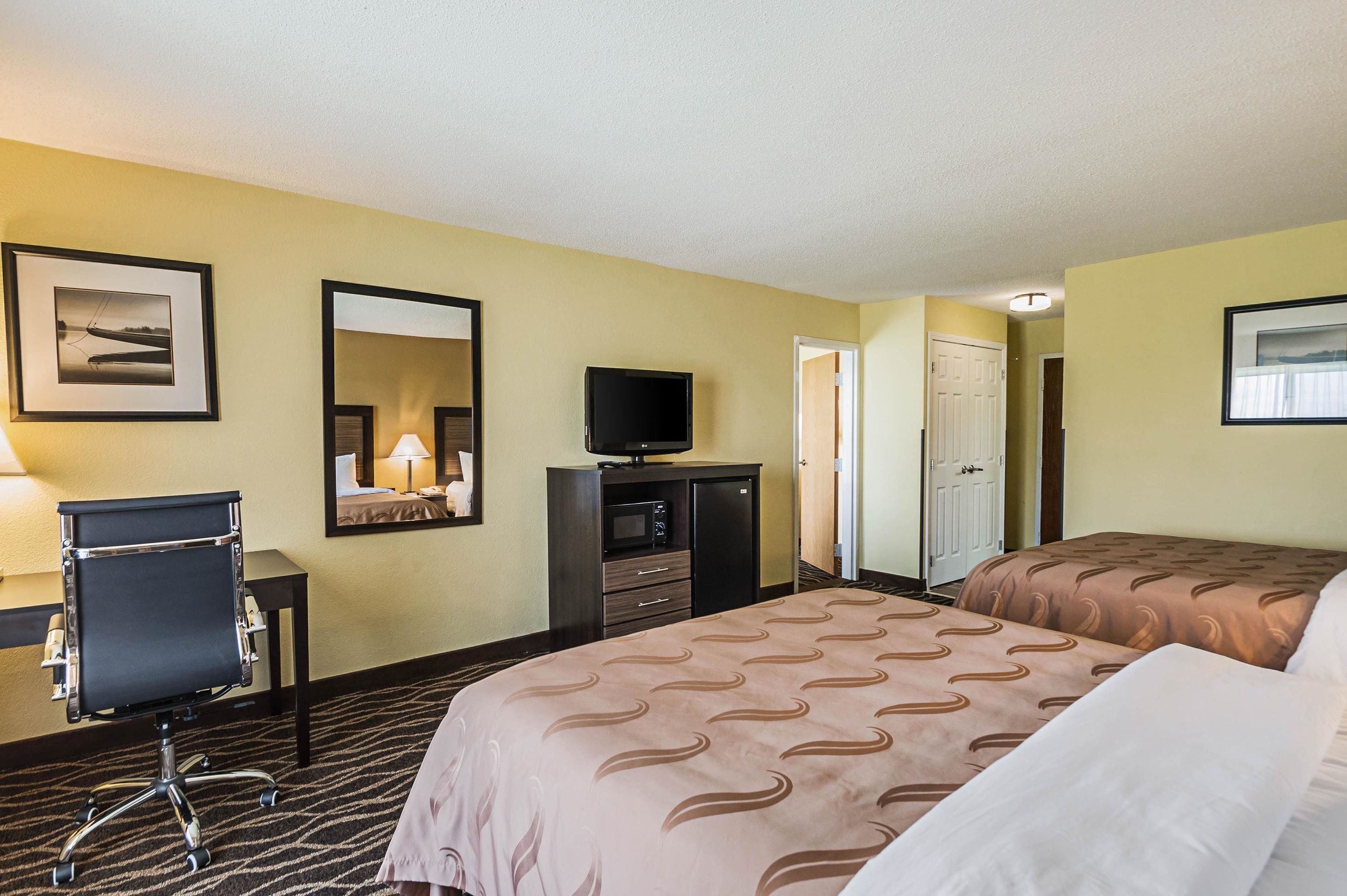 A hotel room with two beds, a desk with a chair, a television, a microwave, and a door leading to another room.