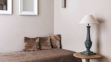 Une chambre à coucher avec un lit, deux tableaux encadrés, une lampe fixée au mur, une table ronde avec une lampe et une tête de lit marron recouverte de tissu.