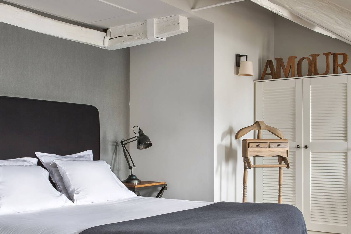 A bedroom with a bed, bedside table, lamp, wardrobe, and a wooden hanger.