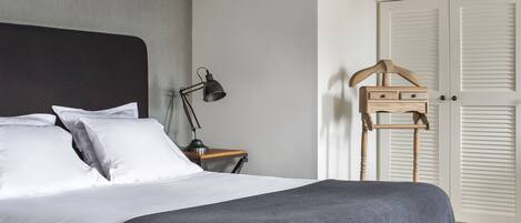 A bedroom with a bed, bedside table, lamp, wardrobe, and a wooden hanger.
