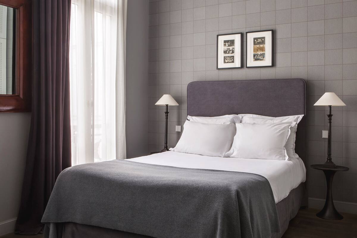 A neatly made bed with a grey bedspread, two bedside lamps, and a headboard.