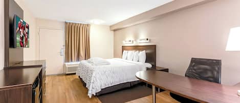 Habitación de hotel con cama, escritorio, silla, televisor y ventana con cortinas.