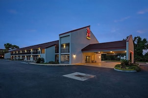 A motel with a large parking lot, a covered entrance, and a sign reading "Red Roof Plus".