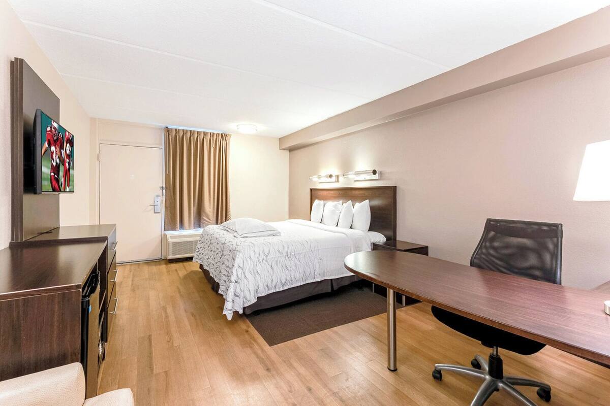 A hotel room with a bed, a desk, a chair, a TV, and a window with curtains.