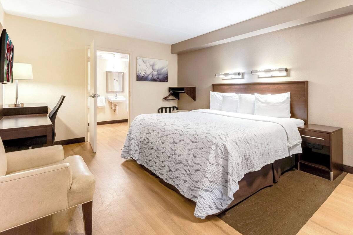 A hotel room with a bed, bedside tables, a desk, a chair, a lamp, a mirror, and artwork on the walls.