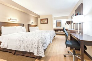 A hotel room with a large bed, a desk with a chair, a mirror, and a wall-mounted lamp. - Red Roof Inn PLUS+ Mt Pleasant - Patriots Point (Mount Pleasant)