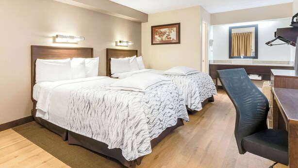 A hotel room with two beds, a desk, and a chair.
