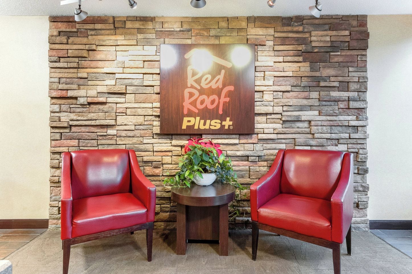 A Red Roof Plus sign, two red leather chairs, and a small table with a potted plant.