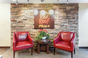 A Red Roof Plus sign, two red leather chairs, and a small table with a potted plant.
