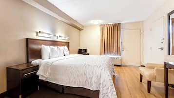 Een hotelkamer met een groot bed, een nachtkastje, een stoel, een bureau, een raam met gordijnen en een airconditioning.