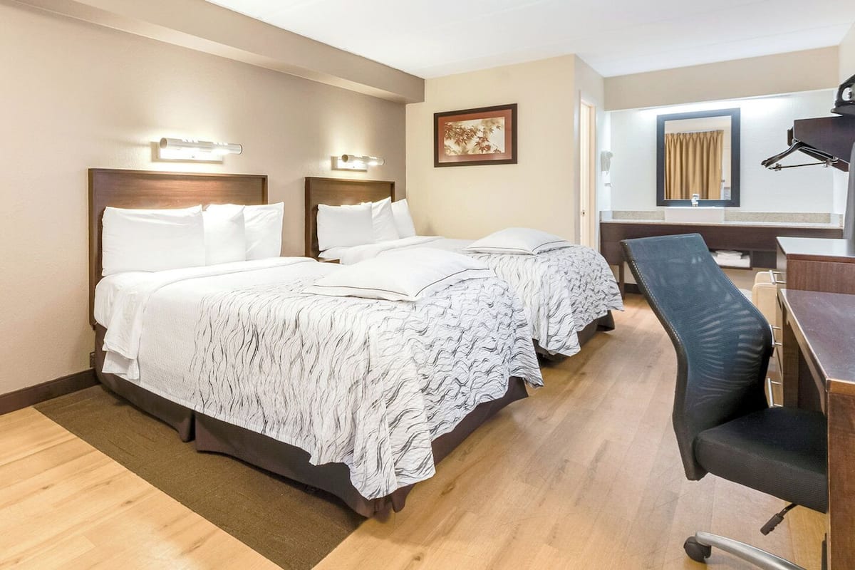 A hotel room with two beds, a desk, and a chair.