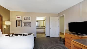 A hotel room with a bed, a desk, a television, and a bathroom visible through an open door.