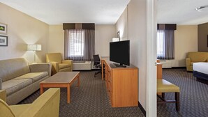 Habitación de hotel con sofá, dos sillones, un escritorio con televisor, una cama y piso alfombrado.