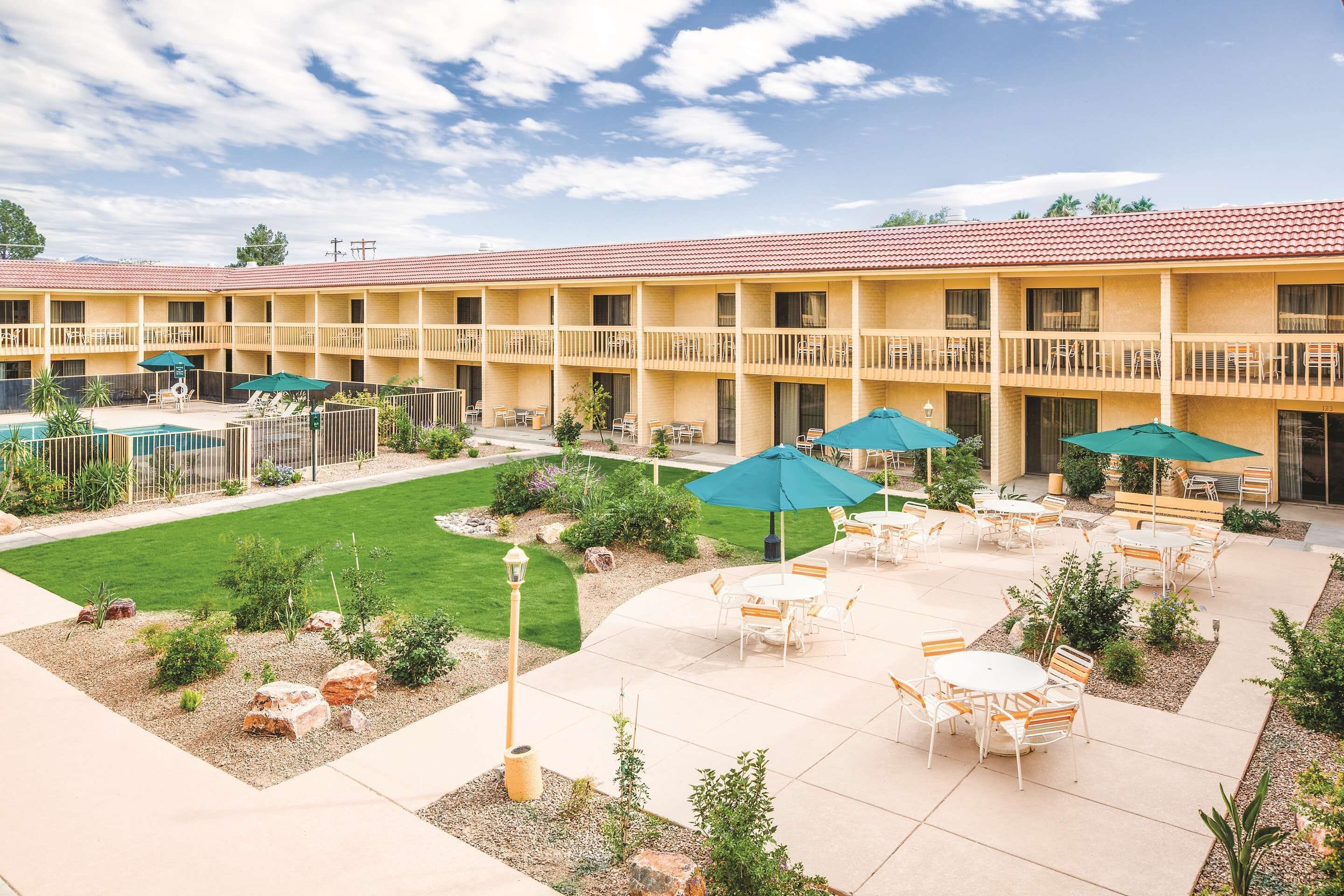 A hotel with a courtyard featuring outdoor seating, a pool, and a well-maintained lawn.