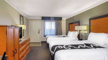 A hotel room with two beds, a wooden dresser, a television, and a window with curtains.