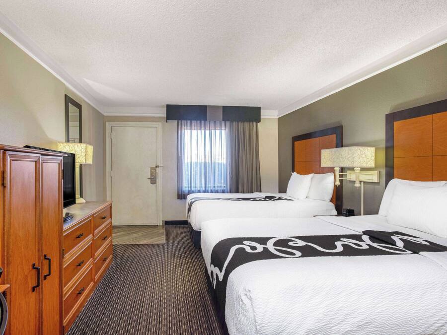 A hotel room with two beds, a wooden dresser, a television, and a window with curtains.
