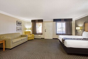 Una habitación de hotel con una cama, un sofá, una silla, una lámpara y una puerta.