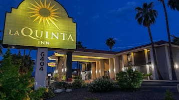 Exterior del La Quinta Inn, con un letrero llamativo, entrada cubierta y palmeras.