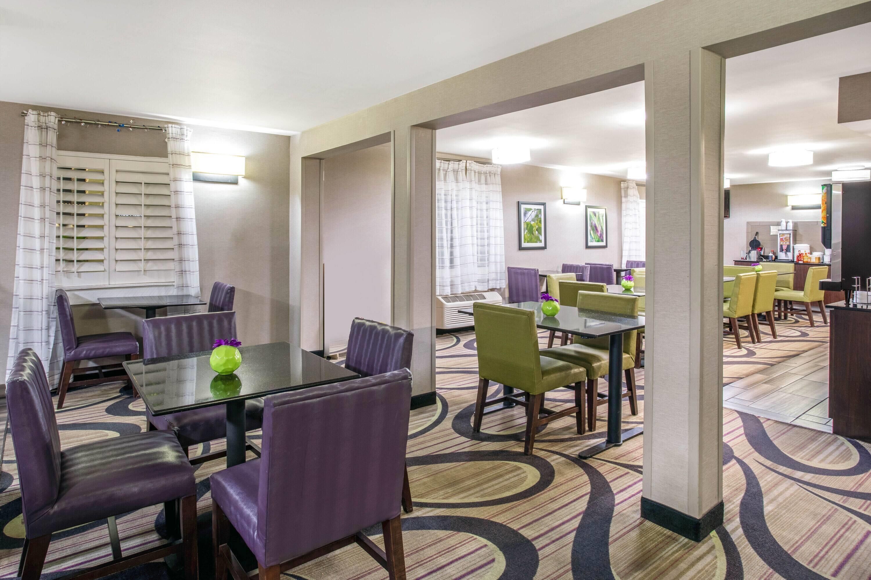 A hotel dining area with multiple tables and chairs, a reception desk, and a view of the kitchen area.