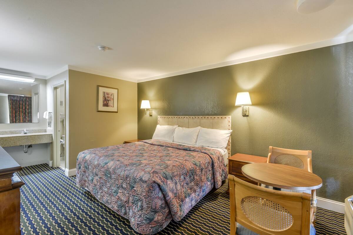 Une chambre d’hôtel avec un lit, une table de chevet, une chaise et une petite table ronde.