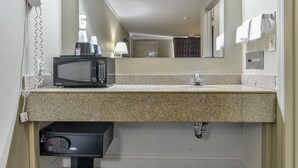 A hotel bathroom with a granite countertop, a black microwave, a hairdryer, and a digital scale. - Wake Inn (Raleigh)