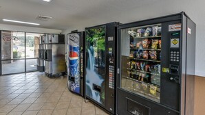 A row of vending machines in a commercial space with a tiled floor and a glass door leading outside. - Wake Inn (Raleigh)