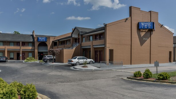 Un edificio de dos pisos con un letrero que dice "Wake Inn", un estacionamiento y un coche blanco estacionado al frente.