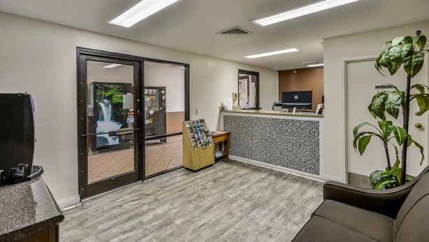 A reception area with a counter, a computer, a small plant, and a door leading outside. - Wake Inn (Raleigh)