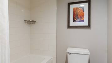 A bathroom with a bathtub, toilet, and a framed picture on the wall.