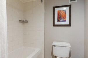 A bathroom with a bathtub, toilet, and a framed picture on the wall.