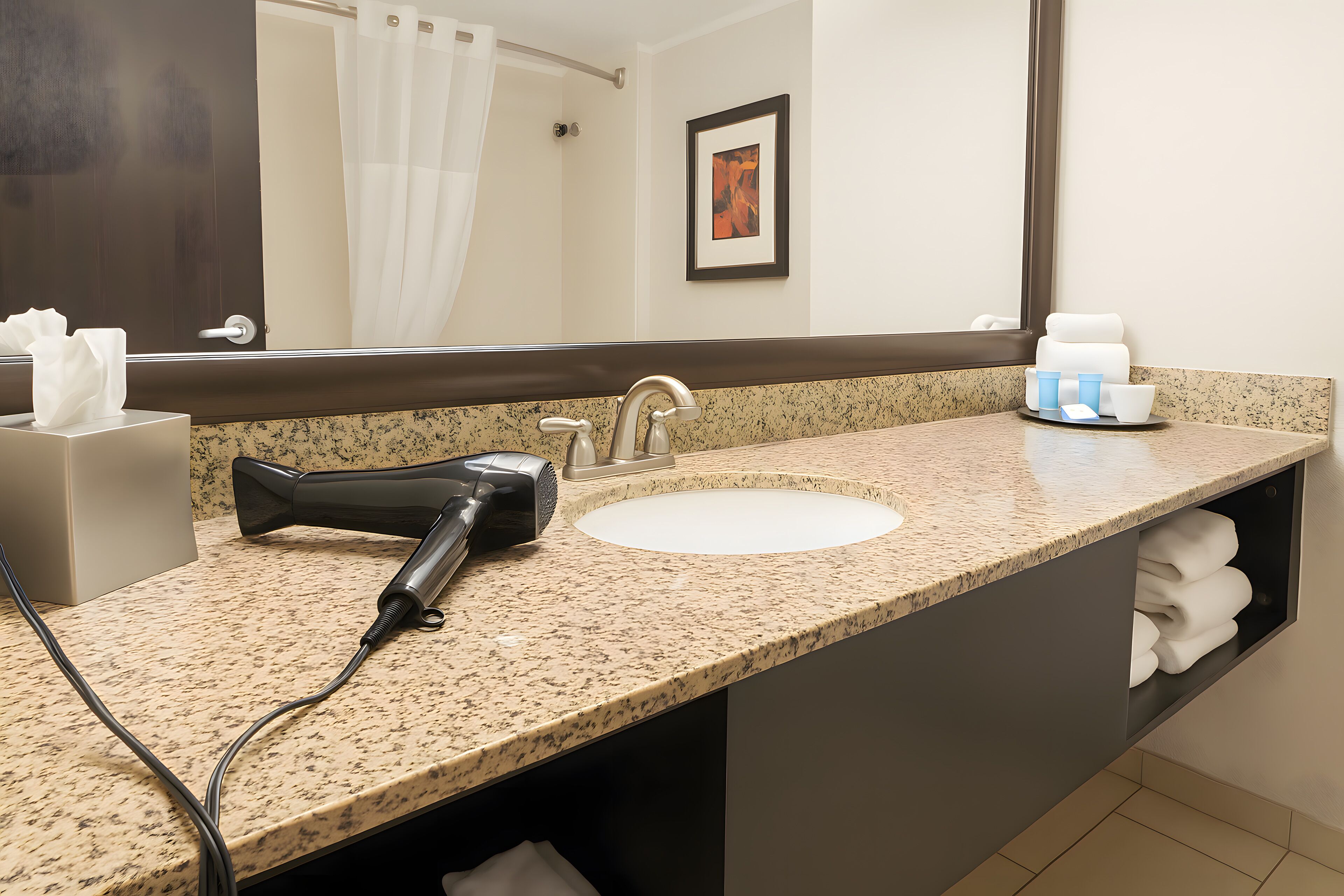 A bathroom with a granite countertop, a sink, a hairdryer, and a towel rack.