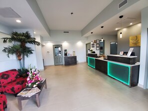 A hotel reception area with a modern design, including a reception desk with green lighting, a large potted plant, and a red sofa with floral upholstery.